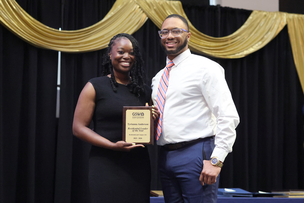 Student poses with plaque next to staff member
