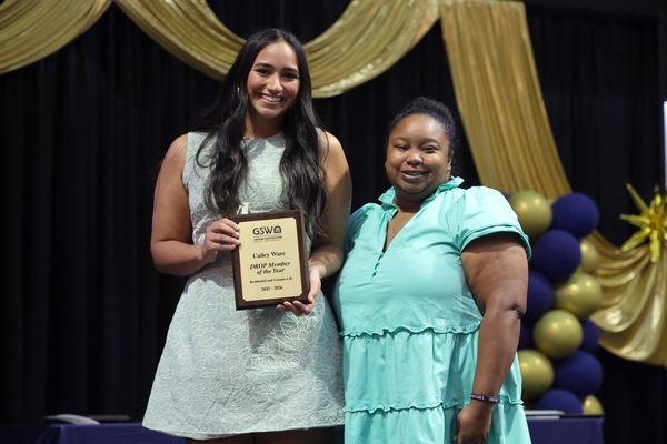 Student poses with plaque next to staff member