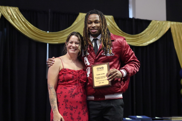 Student poses with plaque next to staff member
