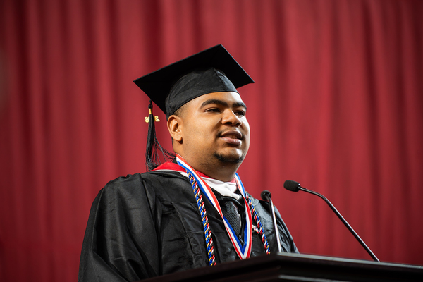 Young man in graduation cap and gown giving a speech