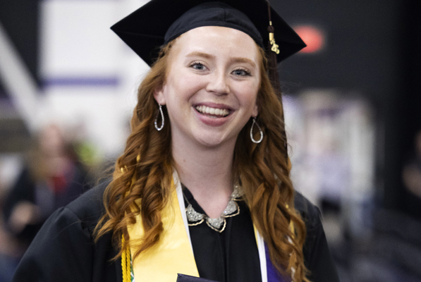 A college student dressed in graduation regalia holding a diploma cover at a commencement ceremony.