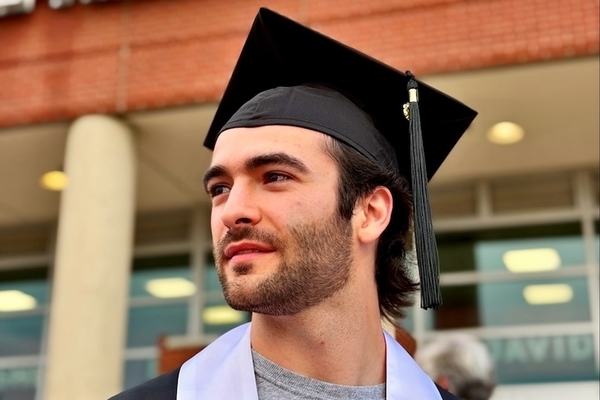 Student wears cap and gown and stands in front of building on university of arkansas campus