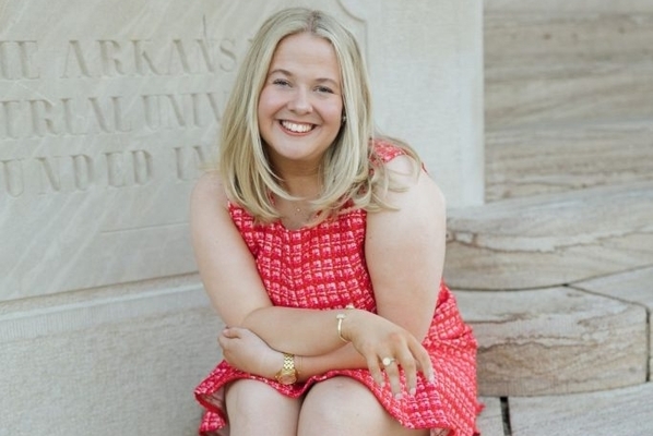 student wearing a red dress and with blonde hair sits on a marble staircase. 