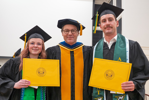 Students holding their certificates wearing their cap and gown, smiling for a picture