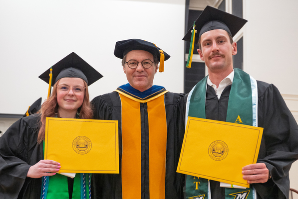 Students holding their certificates wearing their cap and gown, smiling for a picture. 