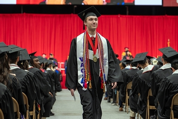 jacob holmes in cap and gown walks down an aisle of students at commencement ceremony