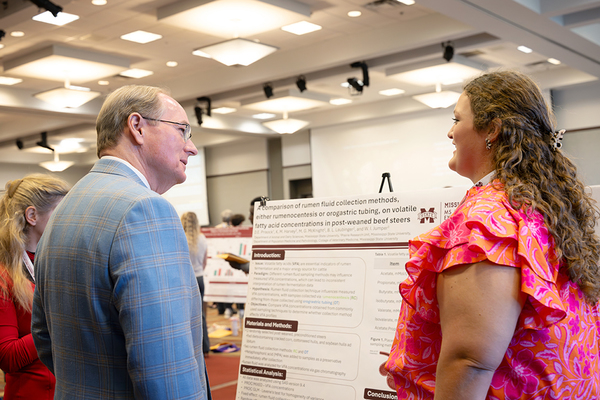 Dru Prisock stands in front of a poster board and describes her research to MSU President Mark E. Keenum.