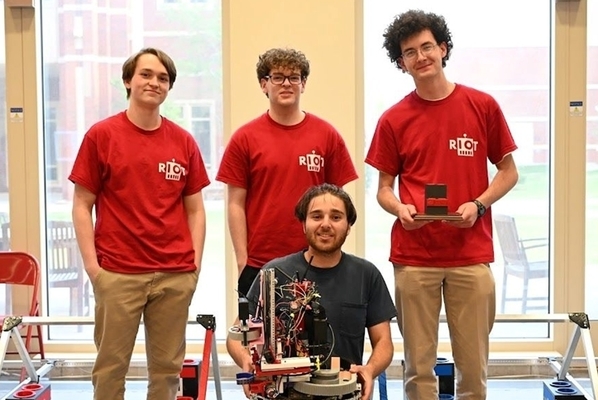 Students stand in a group wearing red tshirts and khaki pants holding their robot.
