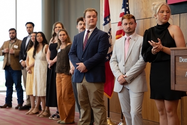 Students stand on a stage dressed up and ready to receive awards. 