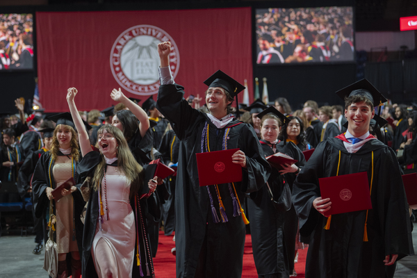 Happy students smiling and waving while walking out of the event venue holding their degrees