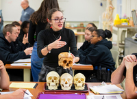 A college student gestures while holding a skull during an archaeology class.