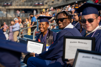 Students wearing dark blue commencement regalia smile and hold framed certificates 