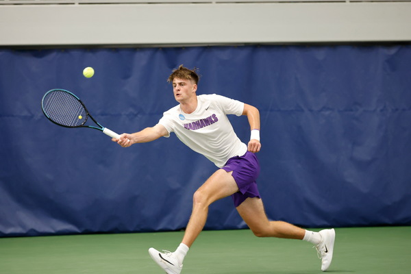 A college tennis player lunging toward a tennis ball.