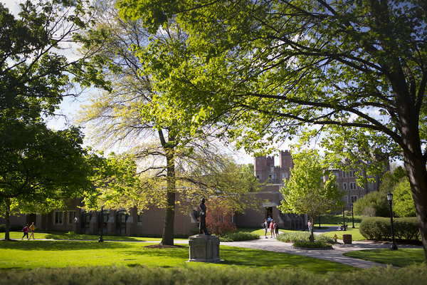 An Elmira College campus building and a couple of walkways with students. The buildings and walkways are surrounded by trees in the spring 