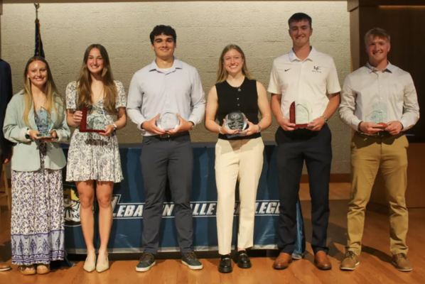 Six students stand on a stage holding their athletic awards.