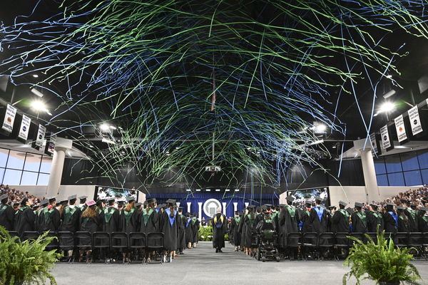 Streamers flying in the Centennial Center at commencement while graduates look up wearing caps and gowns.