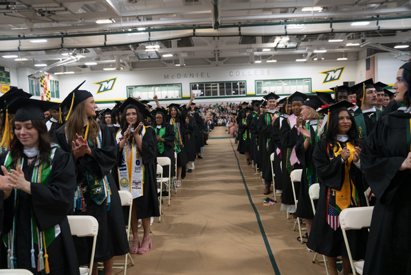 Students standing in their caps and gown clapping their hands. 