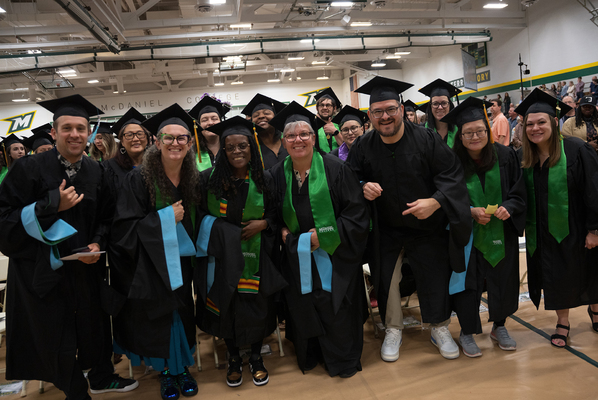 Students standing in their cap and gowns smiling for a picture. 