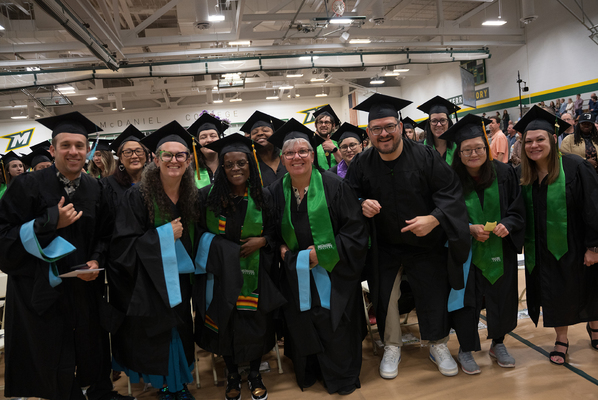 Students standing in their cap and gowns smiling for a picture. 
