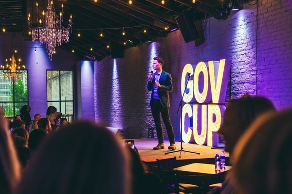 student stands on stage with microphone in front of a crowd with a Gov Cup sign in the background