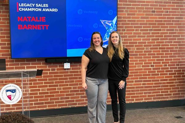 Two individuals pose in front of a screen announcing an award recipient.