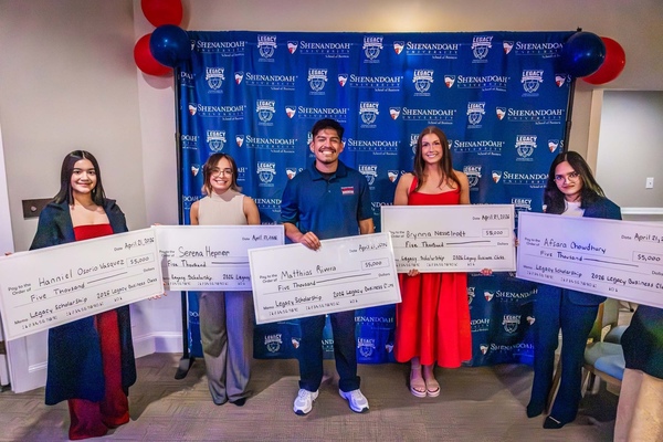 Five recipients of the Legacy Scholarship pose for a photo holding large checks.