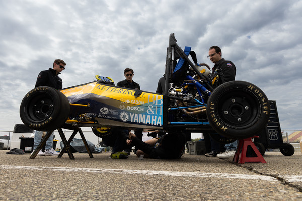 Kettering University Formula SAE team members work on their race car while it sits on stands during competition preparation.