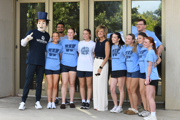 President JuliAnn Mazachek stands with Washburn cheerleaders and the Ichabod mascot outside a campus building during an event.