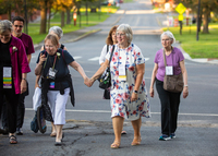 Alumni and emeriti from SUNY Potsdam hold hands and walk across campus at a past reunion event.