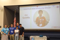 A young student with his family stand in front of a screen with this image and name. He holds up a certificate of achievement.