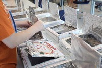 A young person in an orange shirt demonstrates how to use a solar oven made from a pizza box.