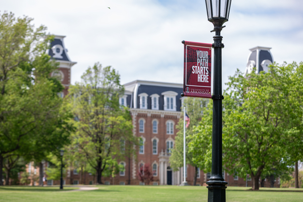 A light pole with a banner that says "Your Path Starts Here" stands in front of Old Main on the University of Arkansas campus. 