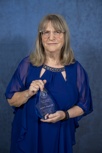 Laura Rozell holds her SUNY Canton Hall of Fame trophy in front of a blue backdrop. 