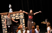 A girl portraying Cinderella throws out her arms and smiles toward the sky, as children gather around her.