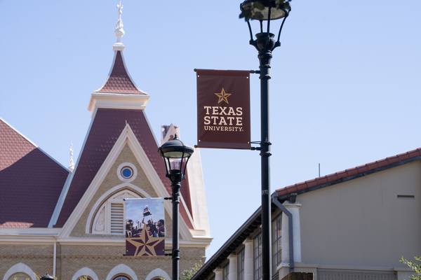 A banner with the Texas State Logo in front of the historic Old Main building. 