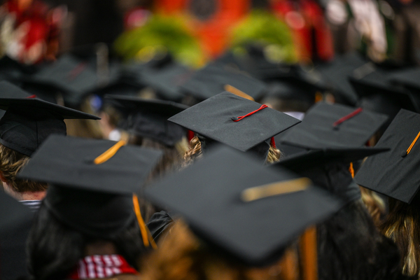 A photo of students sitting during the graduation ceremony with a focus on the back of their graduation caps with the stage in the distance.