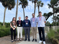 Four students and one faculty member standing in front of palm trees
