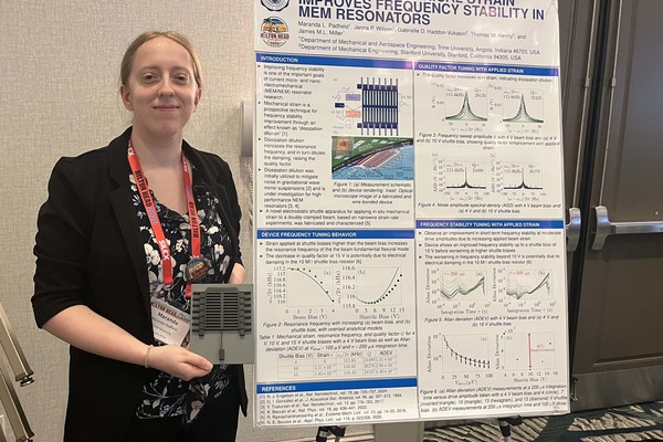 Student holding device and standing to left of research poster