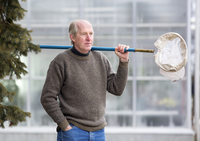 William Romey poses with a net used for catching insects as part of his research in a greenhouse at SUNY Potsdam.
