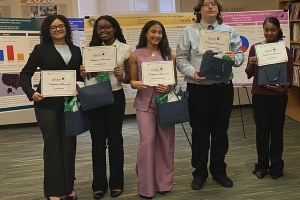 Five individuals stand together holding certificates of accomplishment at an event at Russell Sage College, surrounded by informational posters.