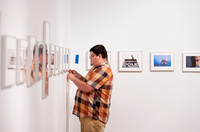 A student hangs framed photography as part of a gallery exhibition.