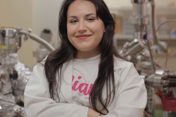 female student in lab coat and Miami University t-shirt standing in laboratory with arms crossed 