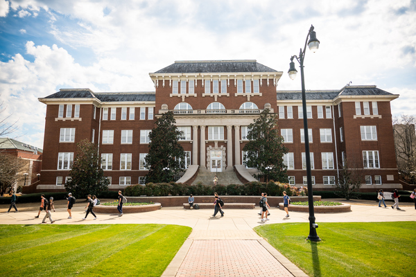 Students walk in front of a large building on a sunny day.