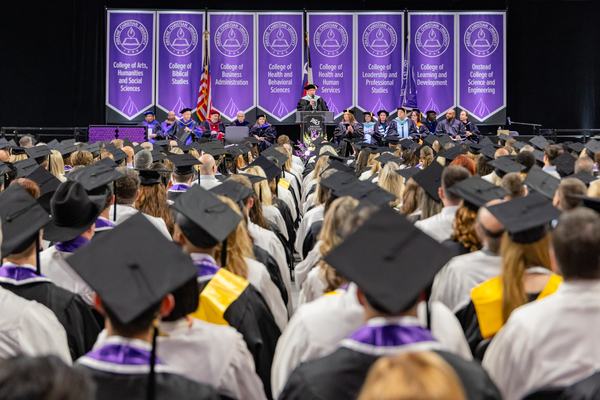 May Commencement at ACU: graduates in caps and gowns in the foreground with speaker on stage in the background
