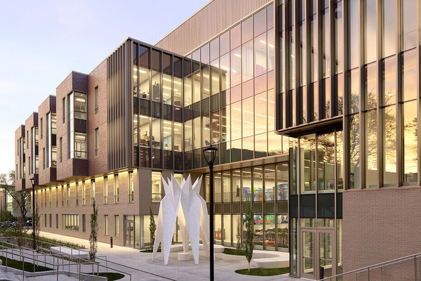 Exterior photo of the west side of Carolyn Pope Edwards Hall, a brick building with numerous windows and a white paper-plane sculpture in front.