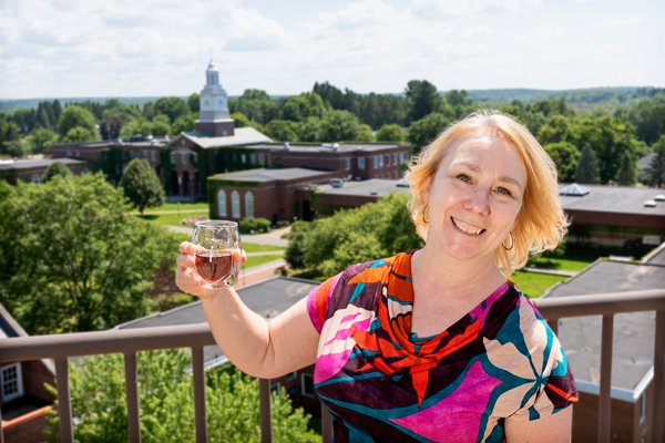 SUNY Potsdam Provost Dr. Susan Perkins '93 raises a glass from the Raymond Hall eighth floor lounge and balcony, where she will lead “A Natural History of Rum: Tasting and Talk” on Thursday, Aug. 20. The 21+ event will feature guided rum tastings, light food pairings, and an exploration of the history and culture of rum. 