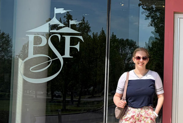 Emma Howson in front of a Pennsylvania Shakespeare Festival glass logo
