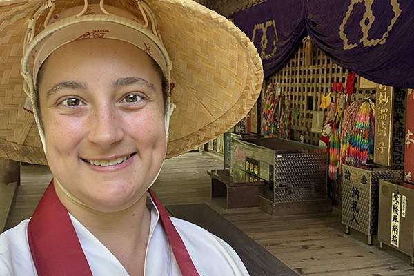 A woman wearing the traditional hat and clothing of Japan's Shikoku Pilgrimage, consisting of a straw hat, white top, and red sash over her shoulders