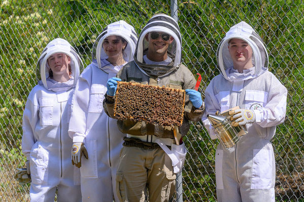Manuel Giannoni-Guzmán, assistant professor of biology at MTSU holds up a beehive frame laden with honeybees alongside students.