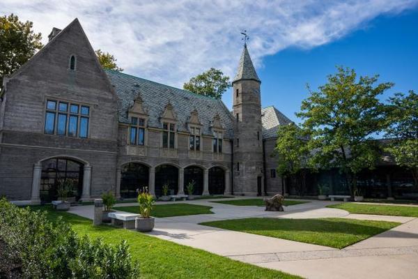 Kean Hall, historic stone brick building with peaks, large windows and arched doorways on a blue-sky day. 